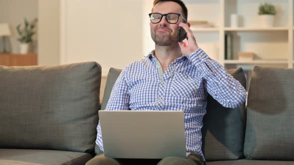 Cheerful Man with Laptop Talking on Smartphone  alt