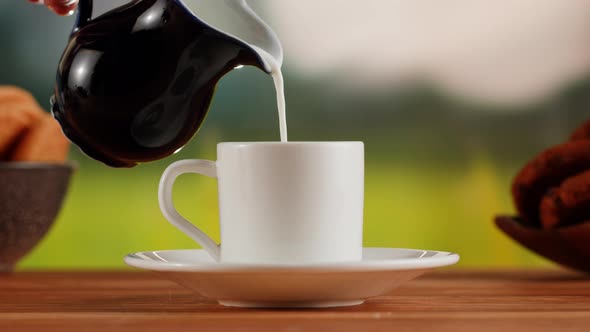 Pouring Milk Into Hot Coffee in White Cup on a Wooden Table alt