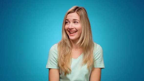 Young Pretty Woman Laughing and Gossiping Pointing Aside Against Blue Background alt