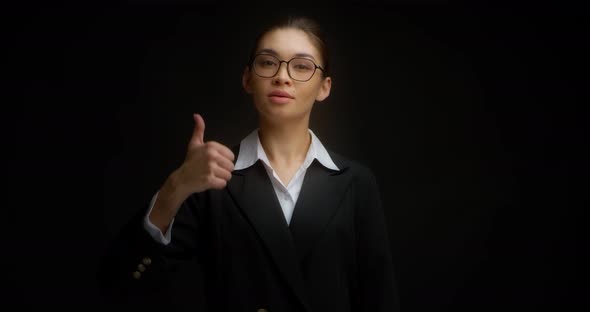 Serious Asian Woman in Business Clothes and Glasses Gives a Thumbs Up