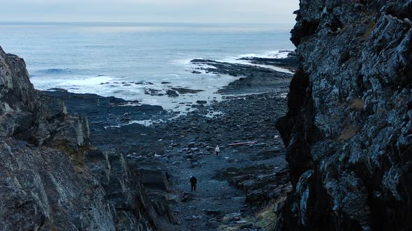 Two people walking on a rocky beach in cold weather. Aerial view.