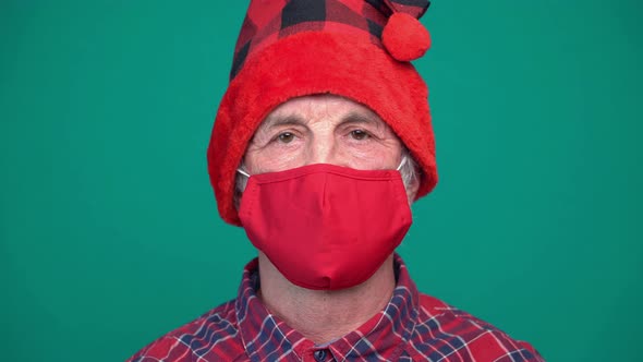 Portrait of Mature Man with Red Medical Face Mask and Santa Hat Looking at Camera
