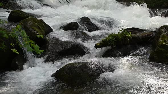 Slow motion of wild clear mountain river , stream flowing through rocks.