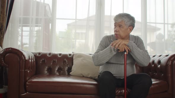 Alone senior man sitting on couch with walking stick