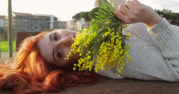 Young Girl Lying on a Table with Yellow Flowers in Her Hand Smiles alt