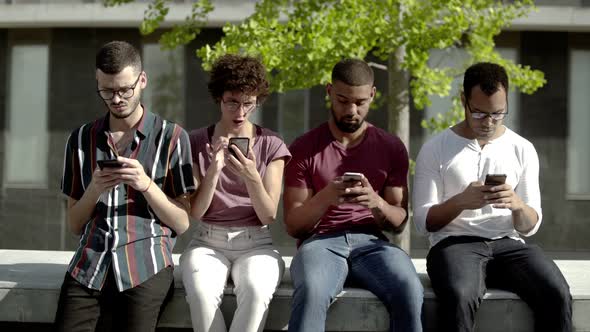 Front View of Focused Friends Using Smartphones in Park  alt