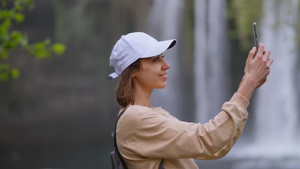Attractive Smiling Woman Tourist Making Selfie on Mobile Phone on Waterfall Background in Antalya alt