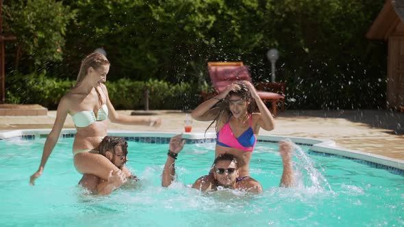 Two Attractive Caucasian Females Sitting on Two Male's Necks Splashing Water Playing in Pool alt