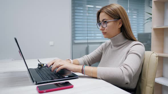 Cute Woman Working at a Laptop with Glasses Typing Text in the Office Employee at Work on the alt