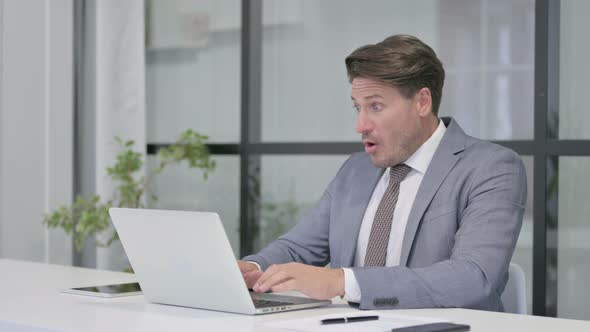 Middle Aged Man Reacting to Loss While using Laptop in Office alt
