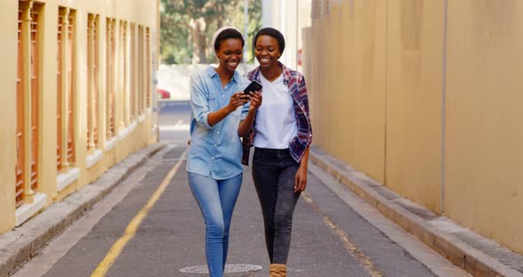 Twin sisters using mobile phone while walking in the city 4k