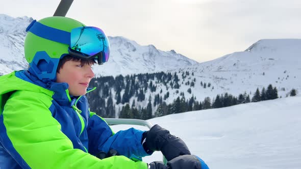 Handsome Boy with Ski Going Up on Chairlift in Mountains alt