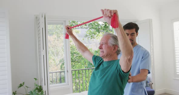 Slow motion of senior man exercising with resistance band by male physiotherapist at retirement home alt