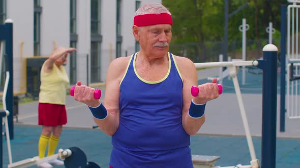 Senior Man Grandfather Doing Training Weightlifting Exercising with Dumbbells on Playground in Park alt