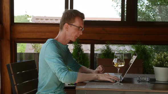 Man Wearing Glasses Using Laptop, Sitting In Cozy Armchair On The Terrace
