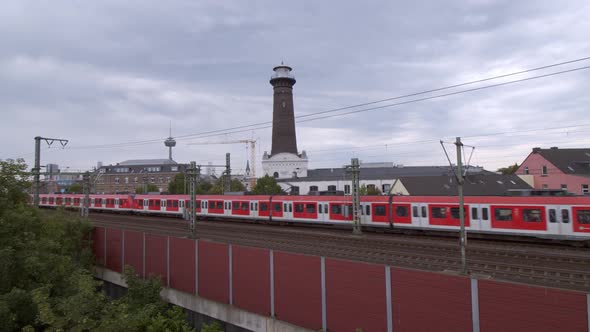 Cologne Ehrenfeld, Germany 2022 - Red commuter train passes with tower in the background on a cloudy alt