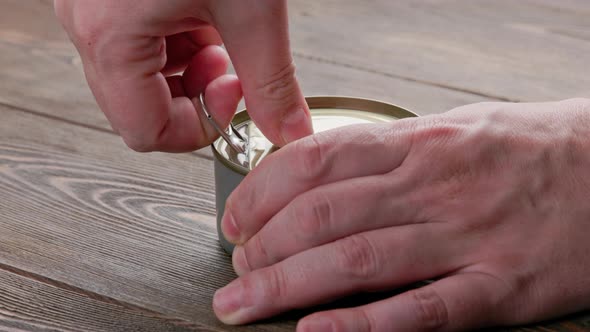 Caucasian Hands Opens Tin Can with Pull Ring on Wooden Surface