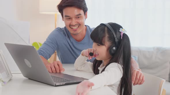Asian little young girl kid use laptop computer learning online class at home with father's support. alt