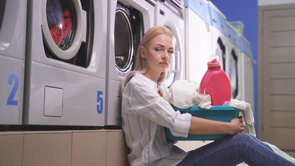Woman Sits on the Laundry Floor Near the Washing Machines