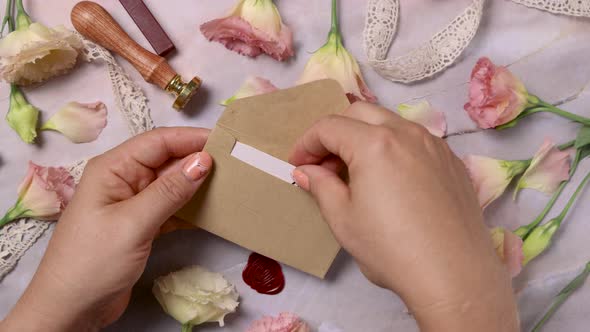 Hands opening an envelope with a MARRY ME card near pink flowers alt