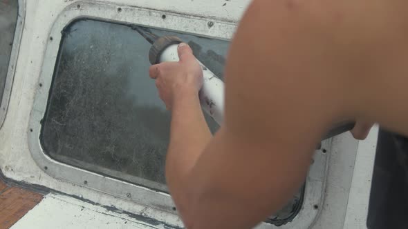 Applying sika flex mastic sealant on bow windows of wooden boat using sealant gun. alt