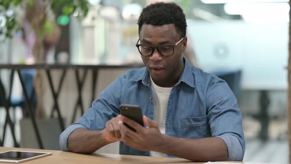 Successful Young African Man Celebrating on Smartphone alt