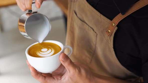 Professional barista pouring steamed milk into coffee cup making beautiful latte art
