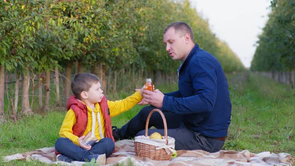 Family Picnic Male Child Takes Juice From His Fathers Hands and Pours It Into Clear Glass alt