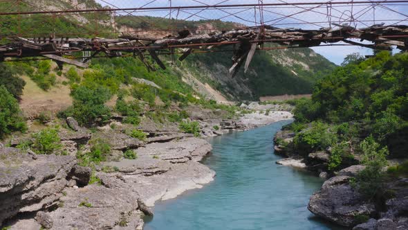 Aerial of woman balancing and walking on dangerous wooden bridge over fresh flowing Vjosa river amid alt