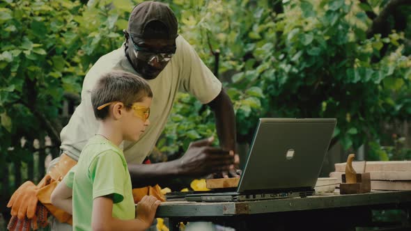 African American Carpenter Shows Boy Tutorial on Laptop