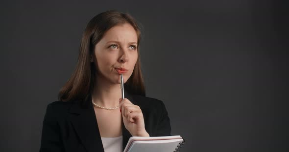 Young Woman in Black Suit Thinks a Little and Writes Her Ideas to the Paper Notepad Making the Notes alt