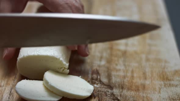 Female Hands Slicing Mozzarella Cheese on a Wooden Cutting Board alt