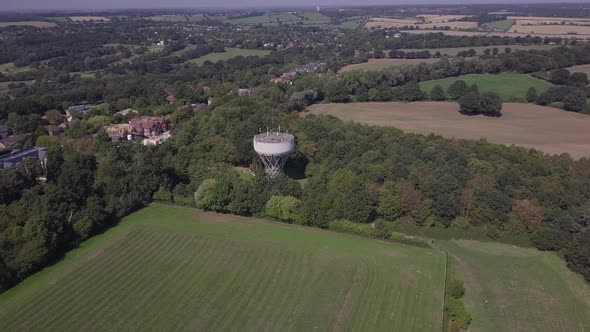 Drone aerial view orbiting water tower in Trent Park North London UK. Big vast green field rural tow alt