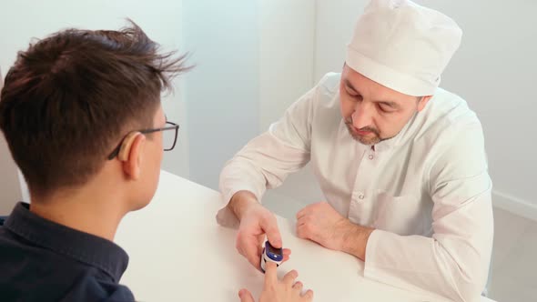 A Doctor in Latex Gloves Using a Pulse Oximeter Measures the Level of Oxygen in the Patient's Blood alt
