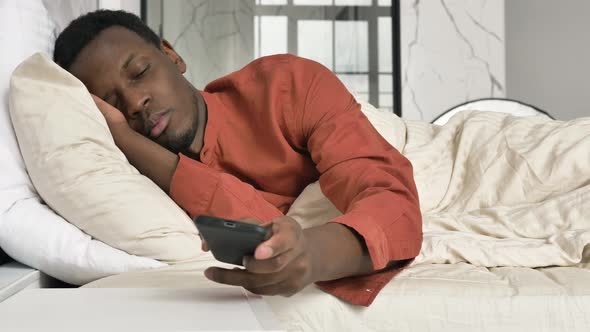 AfricanAmerican Man Switches Off Phone Alarm Clock in Bed alt