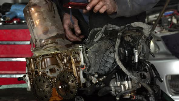 Workshop Master Checks Cylinder Head Of A Dismantled Vehicle Engine Through His Eyes alt