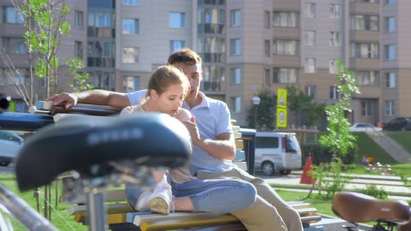 Happy Couple Resting After Cycling on a Bench on a Sunny Summer Day