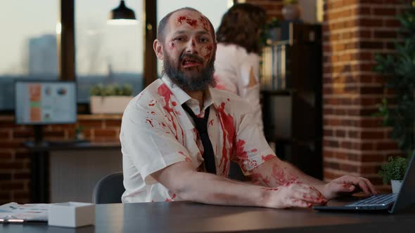 Ugly Dirty Office Zombie Sitting at Desk While Working on Modern Laptop alt