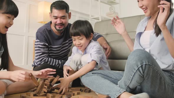 Happy Asian family, parents, and kids are playing with wooden blocks together.