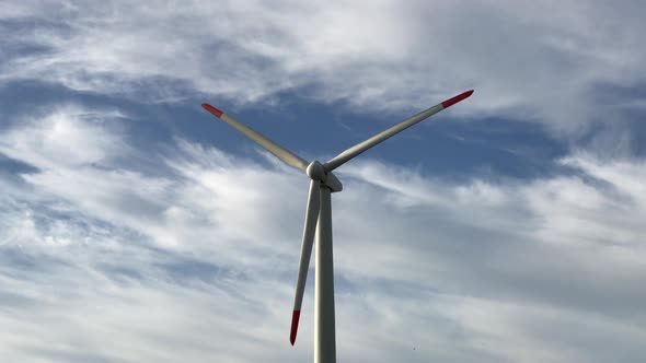Closeup front footage a giant wind turbine with three blades with blue sky and clouds in the backgro alt