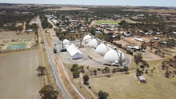 Descending aerial view of grain silos as a trailer full of freshly harvested grain approaches for un alt