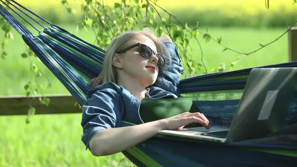 Woman in hammock working with laptop computer in countryside alt