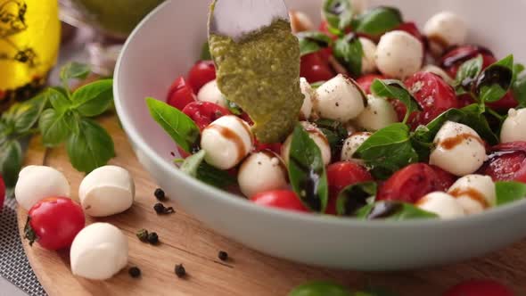 Pouring Pesto Sauce on Caprese Salad with Cherry Tomatoes and Mozzarella Cheese Balls alt