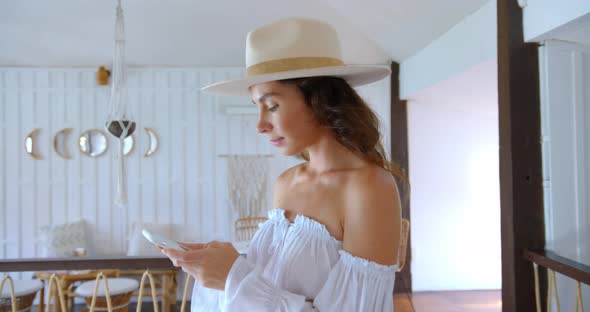 Woman Types the Massage on Smartphone Inside the White Cafe She Wears the Hat and Summer Dress alt