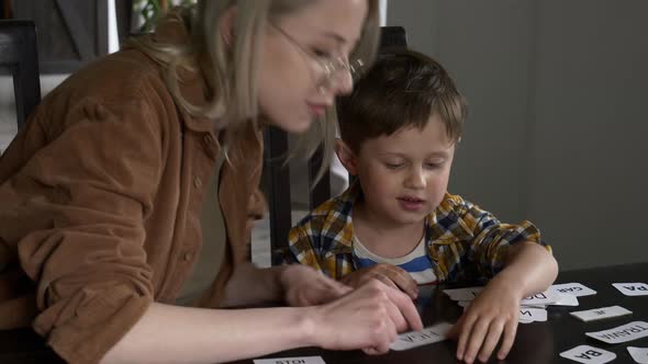 Mom teaches her son how to say the words on the cards at home at the table