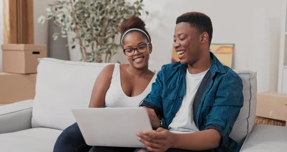 Married Couple is Sitting on Couch in Their New Apartment After Moving in Man is Holding Laptop on alt