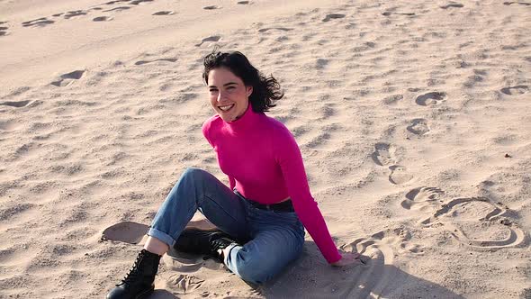 Young Woman Sitting on Sand and Smiling