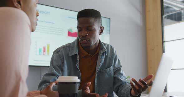 Smiling african american male and female colleague in discussion at meeting using laptop and screen alt