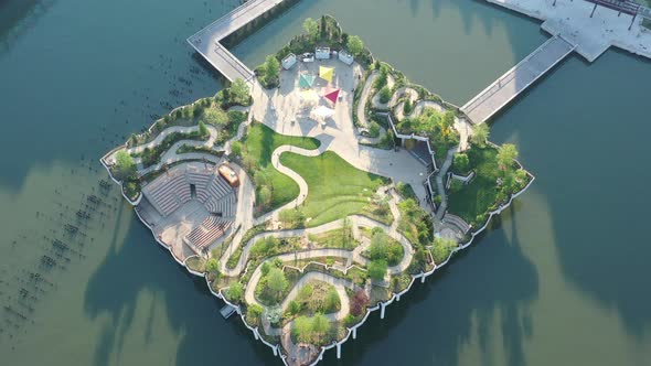 An aerial view over Manhattan's Little Island public green space on a sunny morning. The drone camer alt