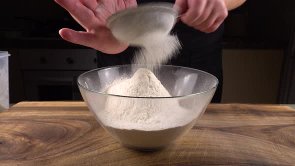 Sifting flour through a sieve into a glass bowl in the kitchen alt